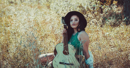 Femme avec un chapeau de festival dans un champ ensoleillé tenant une guitare